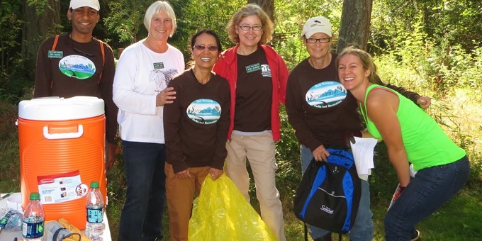 Six Sammamish stewards pause their work for a moment to smile for the camera, one holding a yellow plastic garbage bag.