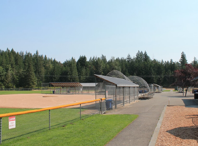 Baseball diamond at Beaver Lake Park surrounded by chain link fence with evergreen trees looming in the background. 