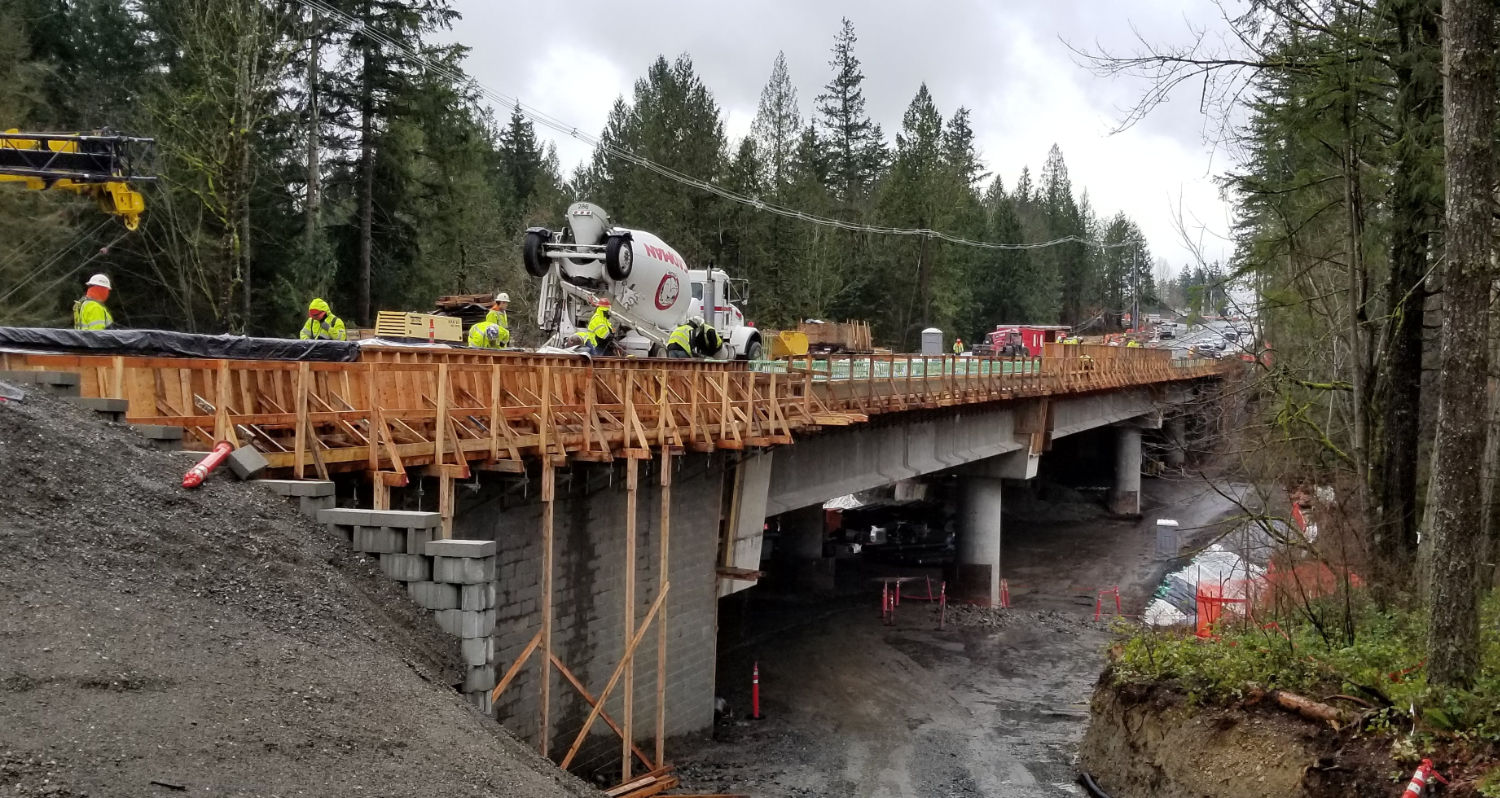 Issaquah Fall City Road bridge from the side, showing  wooden railings along the side of the bridge under construction and concrete pilings beneath
