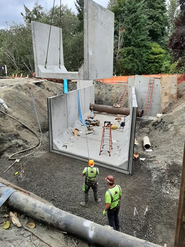 worker uses a guideline to move a culvert bottom into place as it's lowered by a crane beside already placed segments