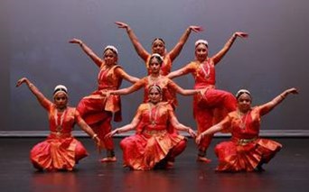 Group of classic Indian dancers posing in bright orange-red costumes.