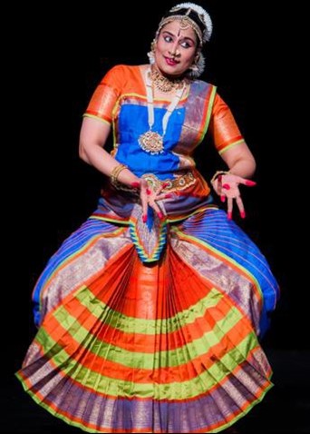 Sandhya Kandadai Rajagopal, performing a classic Indian dance in a colorful orange, yellow, and blue dress.