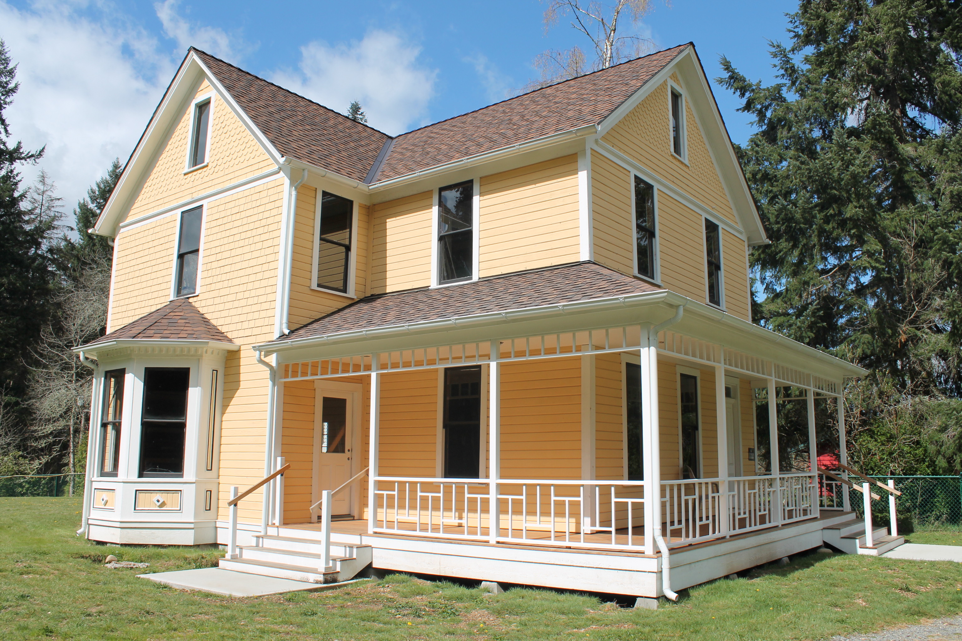 The Reard Freed House exterior after restoration work. It is a yellow 19th century two-story farmhouse with white trim, has a bay window, and a partial wrap-around porch.