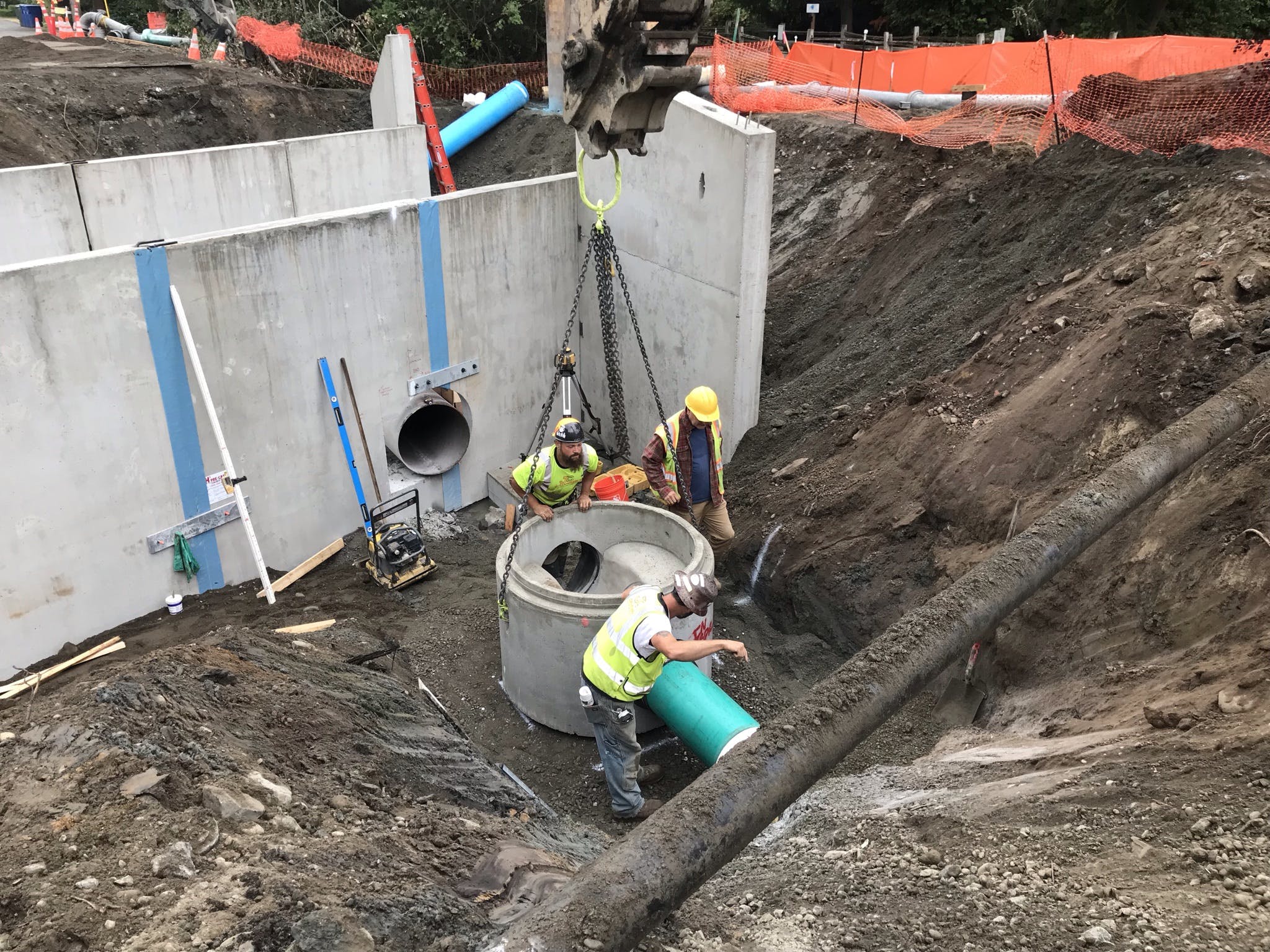 Three crew members coordinate the installation of a sewer manhole on the north side of the culvert at Ebright Creek.  